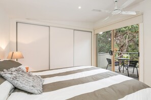 A bedroom with a bed, a ceiling fan, a window, and a view of an outdoor area with a table and chairs.