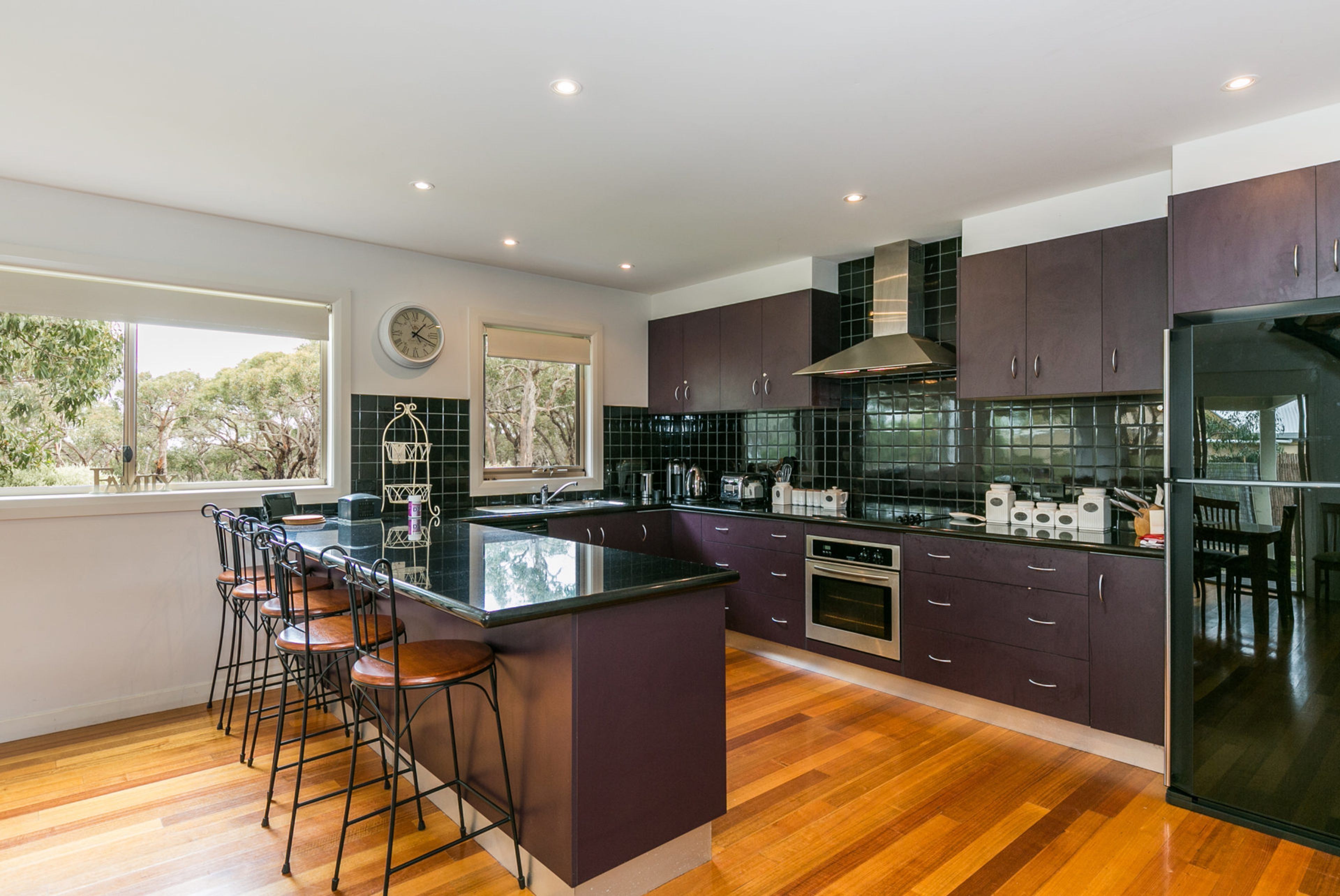 A modern kitchen with a central island, bar stools, a built-in oven, and a large window providing a view of trees.