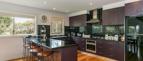 A modern kitchen with a central island, bar stools, a built-in oven, and a large window providing a view of trees.