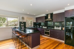 A modern kitchen with a central island, bar stools, a built-in oven, and a large window providing a view of trees.