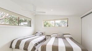Une chambre avec deux lits, un ventilateur de plafond et des fenêtres donnant sur un paysage verdoyant.