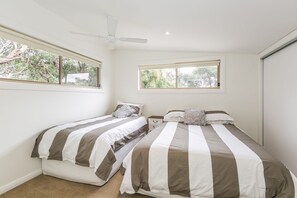 A bedroom with two beds, a ceiling fan, and windows with views of greenery.