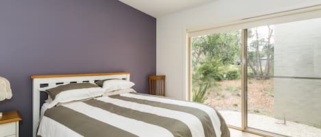 A bedroom with a bed, a nightstand, a chair, and a large sliding glass door leading to an outdoor area.