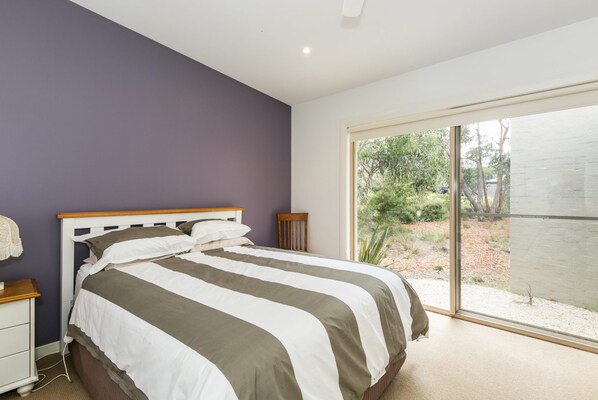 A bedroom with a bed, a nightstand, a chair, and a large sliding glass door leading to an outdoor area.