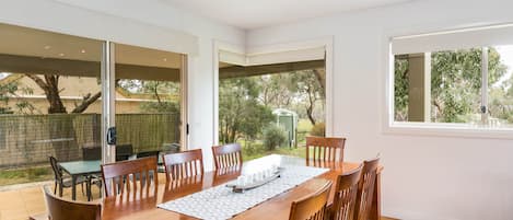 A dining area with a wooden table and chairs, large windows, and a view of the outdoors.