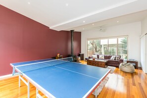 A room with a ping pong table, a sofa, a coffee table, and a large window.