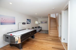 A modern living room with a pool table, a sofa, and a staircase.