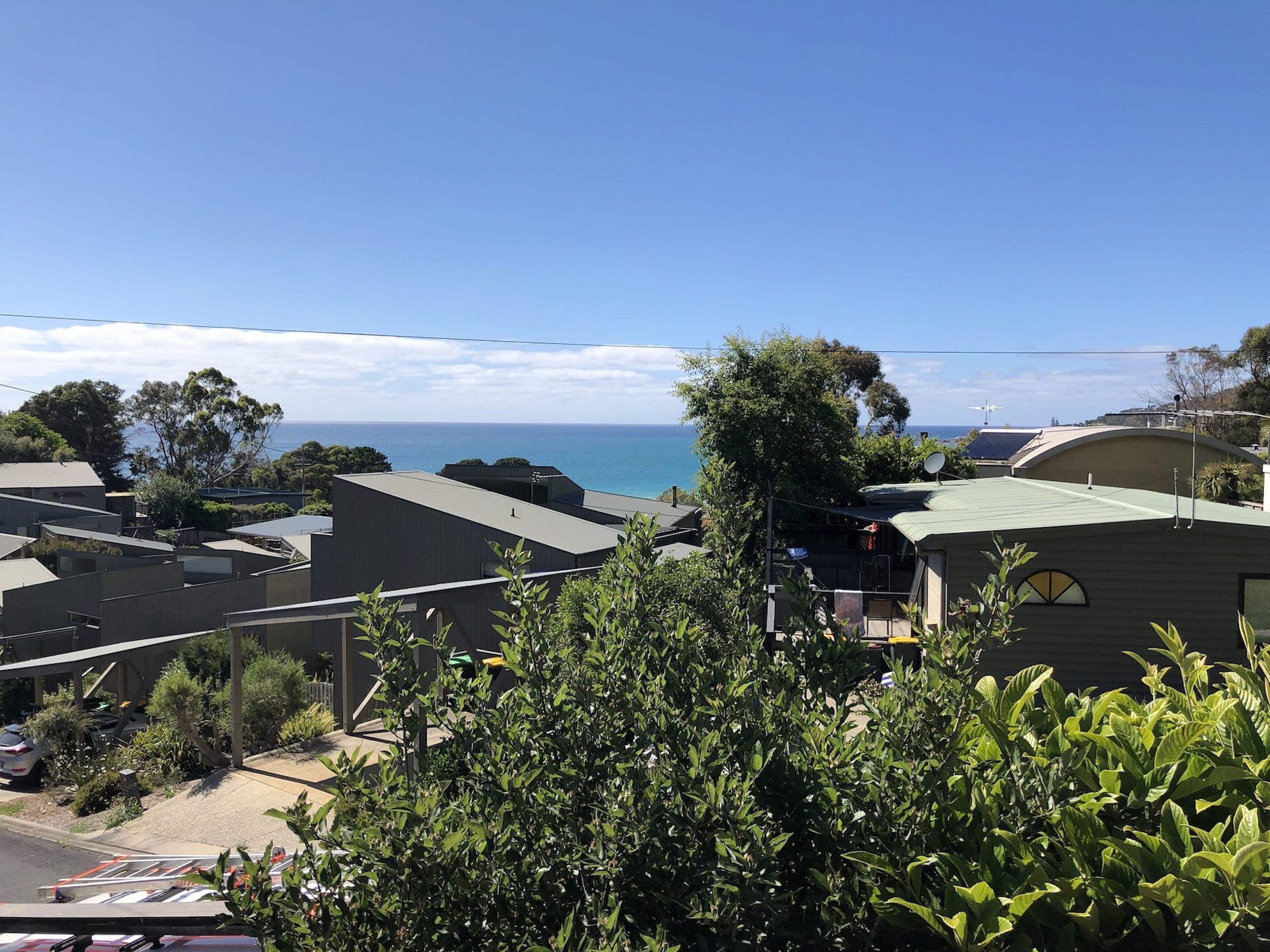 A coastal residential area with houses, a clear sky, and a view of the sea.