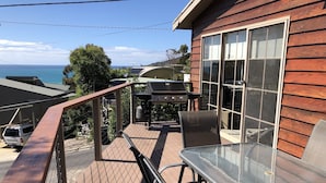 A deck with a glass-top table and chairs, overlooking a scenic view of the ocean.