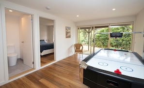A room with a wooden floor, a bed, a window with a view of greenery, and a table hockey game.