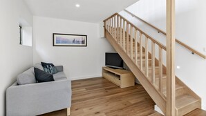 A modern living room with a grey sofa, a flat-screen TV, a wooden staircase, and a framed picture on the wall.