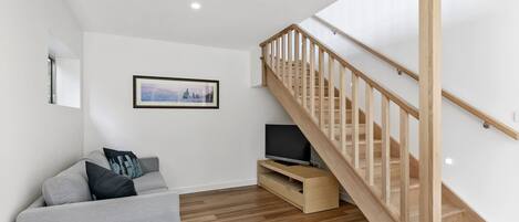 Un salon moderne avec un canapé gris, un téléviseur à écran plat, un escalier en bois et un tableau encadré au mur.