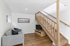 A modern living room with a grey sofa, a flat-screen TV, a wooden staircase, and a framed picture on the wall.