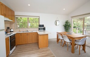 A modern kitchen with wooden cabinets, a built-in stove, a microwave, and a dining area with a table and chairs.