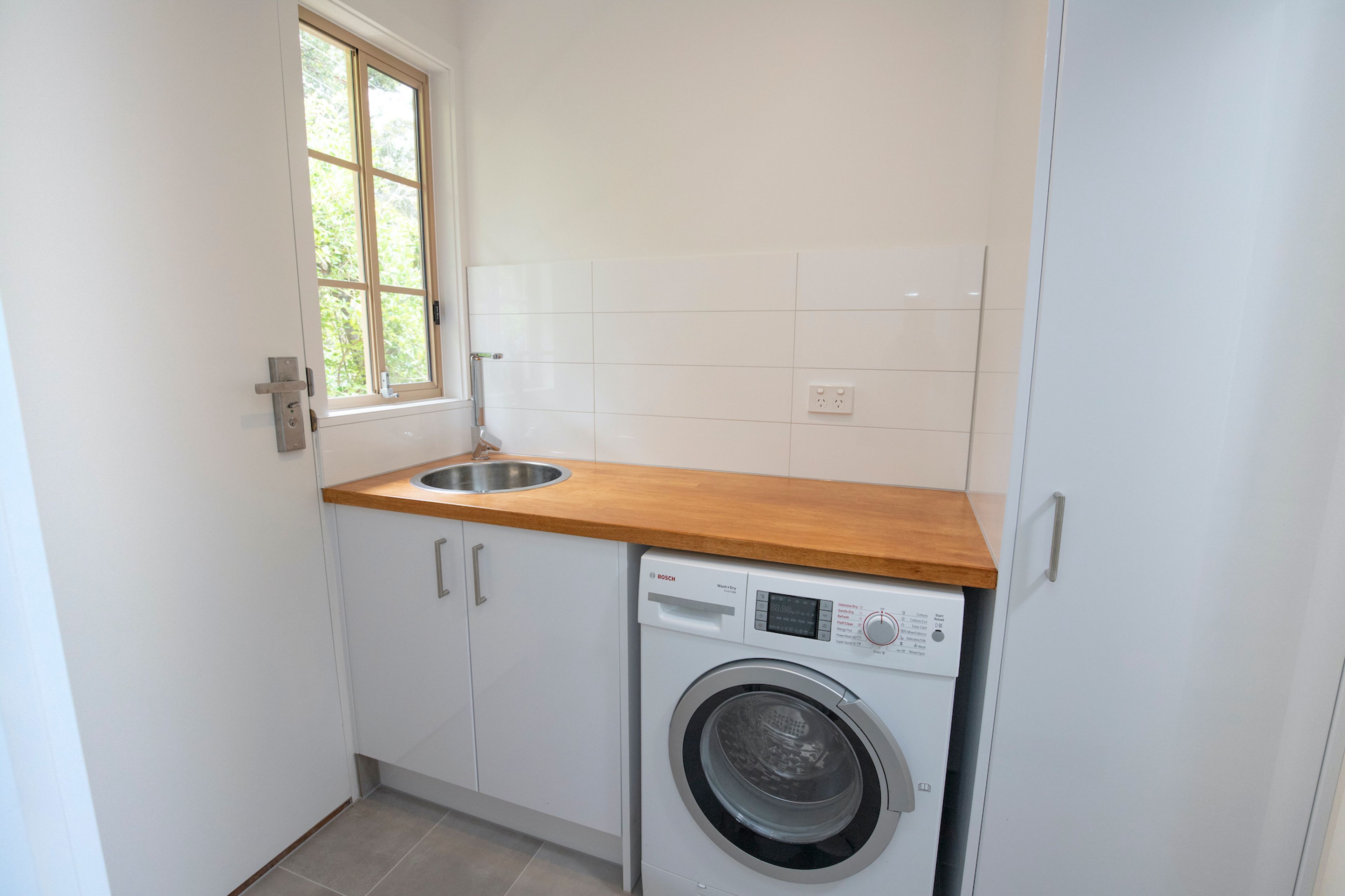Een kleine wasruimte met een wasmachine, een wasbak en een raam.