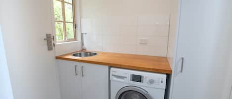 A compact laundry room with a washing machine, a sink, and a window.