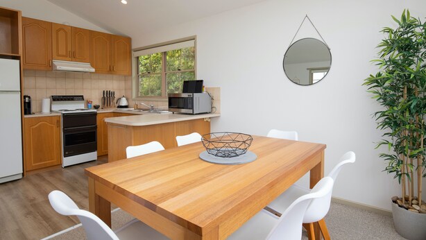 A modern kitchen with wooden cabinets, a dining table with chairs, a microwave, and a large window.