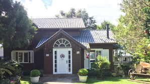 Ein zweistöckiges Haus mit weißer Haustür, einer kleinen Veranda und einem Garten mit Topfpflanzen.