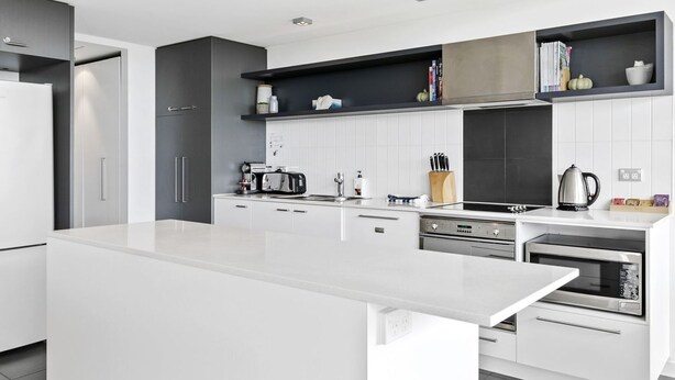 Uma cozinha moderna com armários brancos, uma ilha central e eletrodomésticos embutidos, incluindo fogão, forno e micro-ondas.