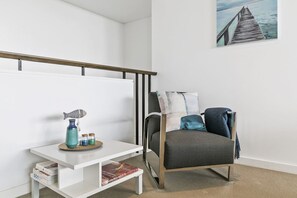 A modern room with a grey sofa, a white side table, a blue vase, and a painting of a pier. - Lorne Chalet Apartment 11 Odyssea (Lorne)