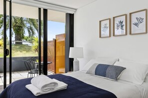 A hotel room with a bed, a chair, a table, and a view of the outdoors. - Lorne Chalet Apartment 11 Odyssea (Lorne)