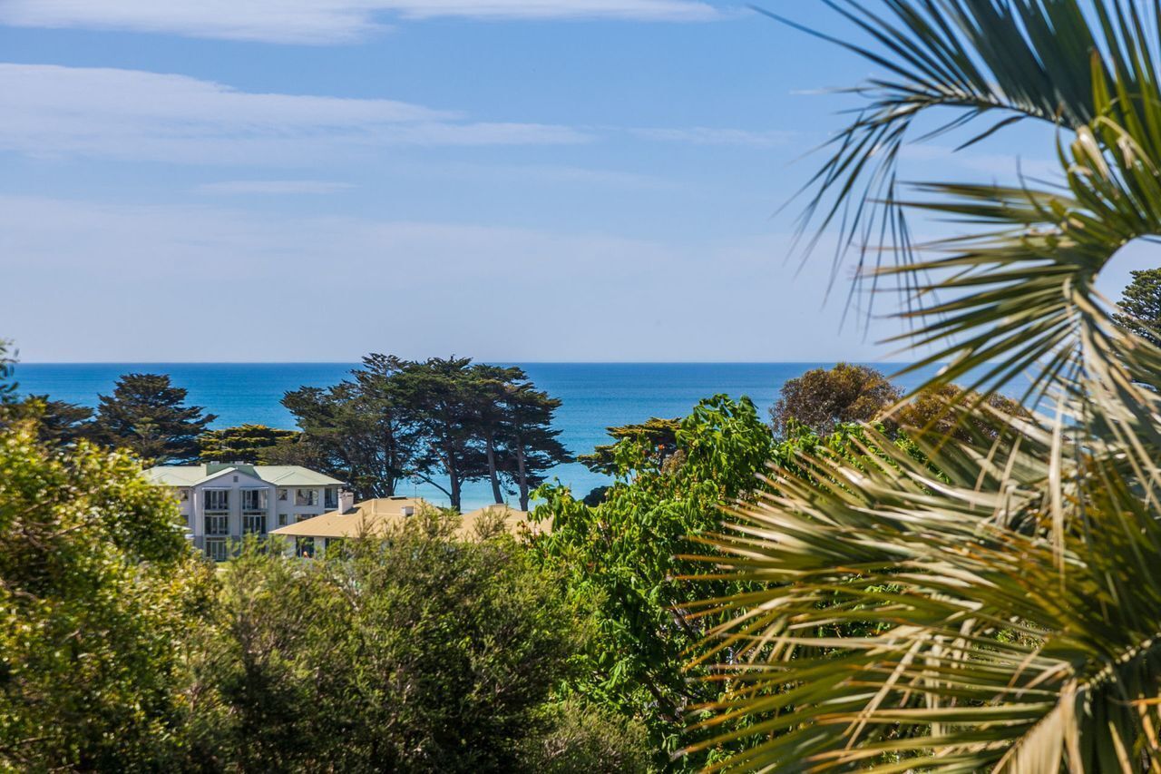 A coastal property with a view of the sea, surrounded by dense greenery and a prominent white building.