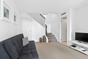 Ein modernes Wohnzimmer mit einem grauen Sofa, einem Flachbildfernseher auf einem weißen Schrank, einer Treppe mit grauen Stufen und einer weißen Tür.