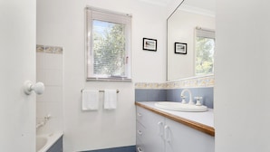 A bathroom with a bathtub, a sink, and a window with blinds. - Sea Loft (Apollo Bay)