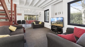 A modern living room with a large TV, comfortable seating, a staircase, and a view of the outdoors. - Sea Loft (Apollo Bay)