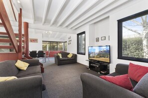 A modern living room with a large TV, comfortable seating, a staircase, and a view of the outdoors. - Sea Loft (Apollo Bay)