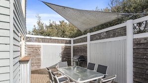 A covered patio with a table and chairs, a barbecue grill, and a white fence. - Sea Loft (Apollo Bay)