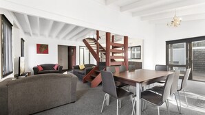 Un vaste espace de vie comprenant un grand canapé, une table à manger avec des chaises, un escalier et une vue sur l’extérieur.