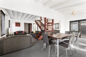 A spacious living area with a large sofa, a dining table with chairs, a staircase, and a view of the outdoors.