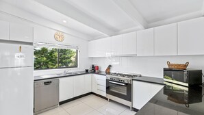Cocina moderna con armarios blancos, estufa a gas, horno, lavavajillas y ventana con vista a zonas verdes.