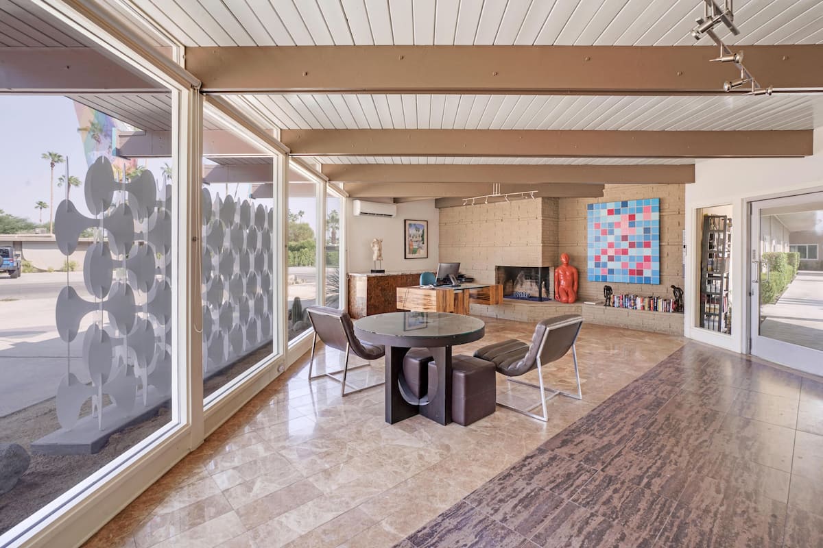 A modern kitchen with a central island, a dining area with a round table and chairs, and a large window providing a view of the outdoors.