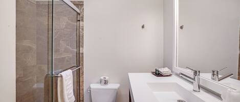 Un baño moderno con cabina de ducha de vidrio, inodoro y tocador doble con un espejo grande.