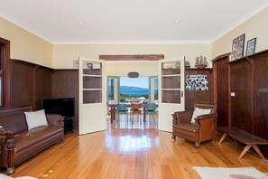 A spacious living room with a wooden floor, a leather sofa, a television, and a view of the sea through an open door. - Callahan (Marengo)