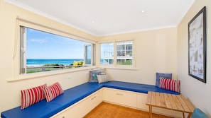 Enjoy ocean views from the bay window in this inviting room, featuring a bench and a wooden table with two chairs.
