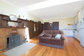 Un salon doté d’une cheminée, d’un plancher en bois, d’un canapé marron et d’un coin cuisine avec des meubles blancs.