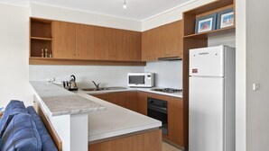 A modern kitchen with wooden cabinets, a white countertop, a microwave, a stove, and a refrigerator. - Apartment 29 Pacific Apartments (Lorne)