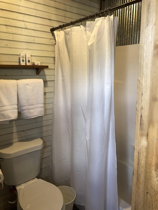 A bathroom with a toilet, a shower curtain, and a shelf with toiletries.