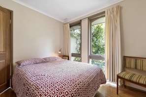 A bedroom with a bed, a chair, a window with curtains, and a view of greenery outside.