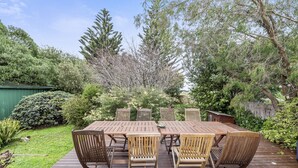 Um deck de madeira com mesa e cadeiras, cercado por vegetação e árvores.