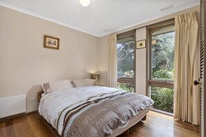Une chambre à coucher avec un lit, une fenêtre avec des rideaux, un tableau accroché au mur et une lampe de chevet.