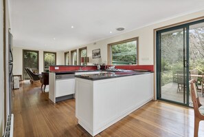 A modern kitchen with a large island, white cabinetry, and a view of the outdoors through large windows.