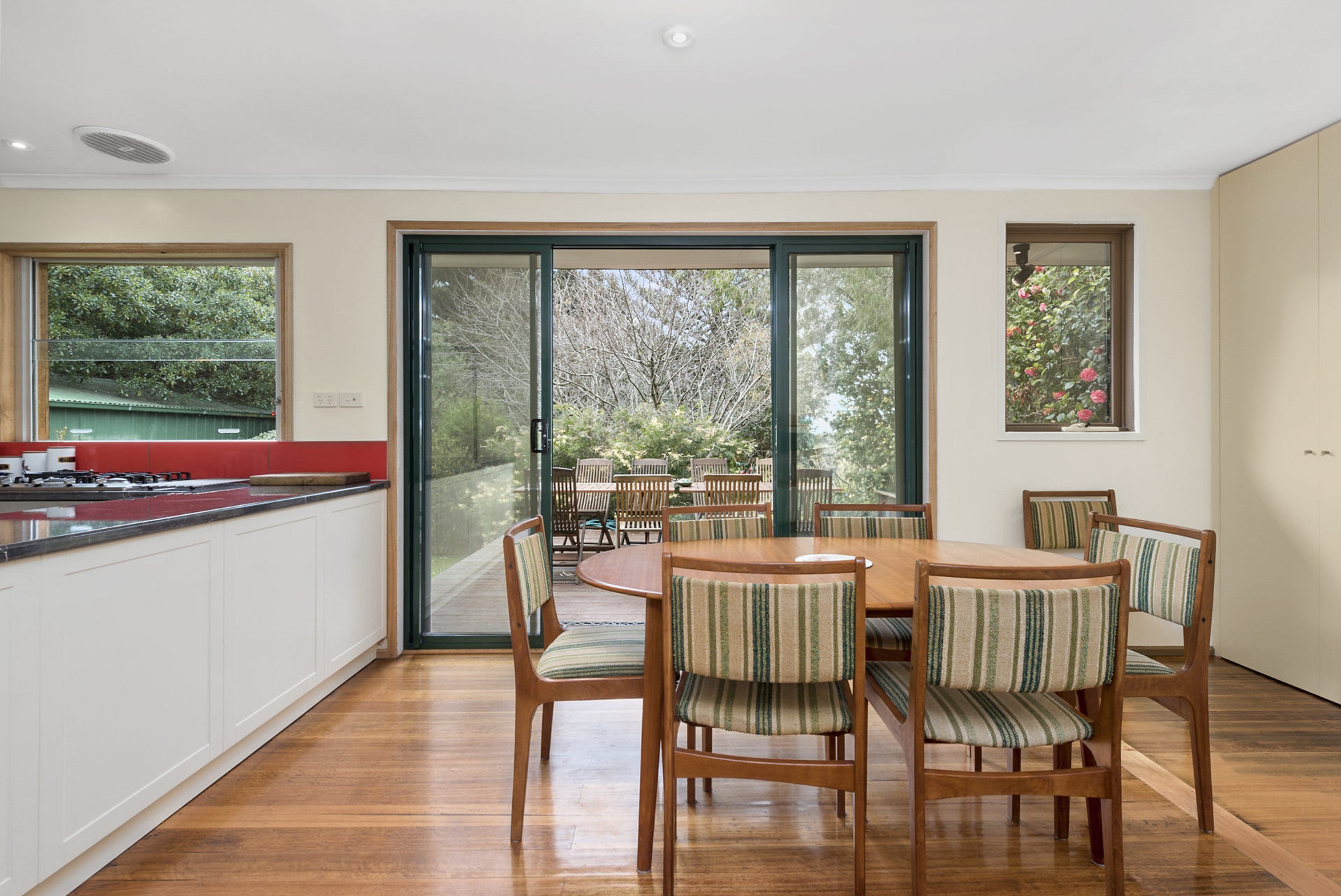 A modern kitchen with a dining area, large windows, and a view of greenery.