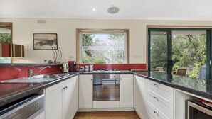 Cozinha moderna com armários brancos, coifa de aço inoxidável e janela com vista para o exterior.