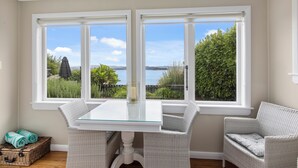 Une pièce avec une table à plateau en verre, deux chaises en osier, une vue sur un lac et un panier en osier contenant des serviettes.