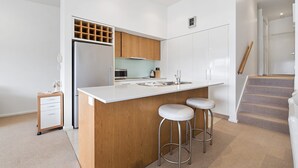 A modern kitchen with a central island, wooden cabinets, stainless steel appliances, and a small bar stool area.