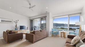 A modern living room with a sofa, armchairs, a TV, and a view of a lake.